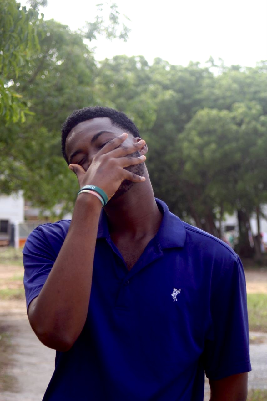 A photo of a person covering their face, dressed in a blue polo shirt.